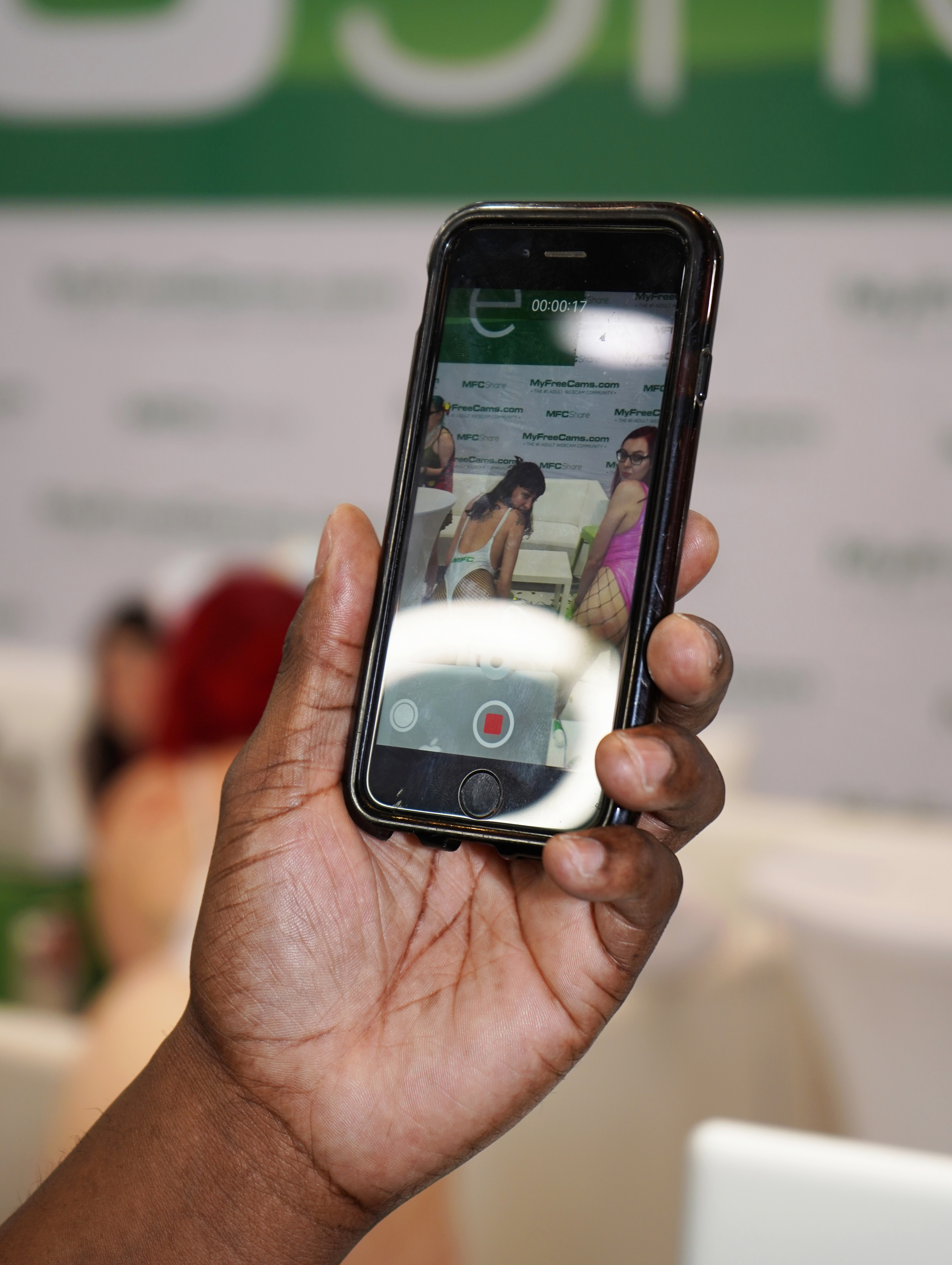 A man's hand holding a cell phone as he takes a photo of two women twerking