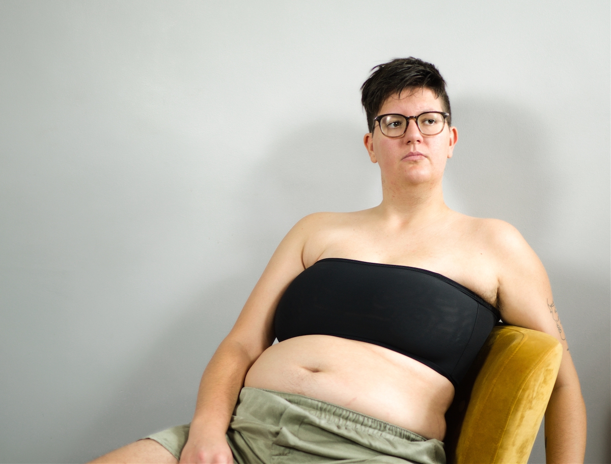 Tilke Wouters wearing a black band binder and boxers and sitting on a yellow chair.