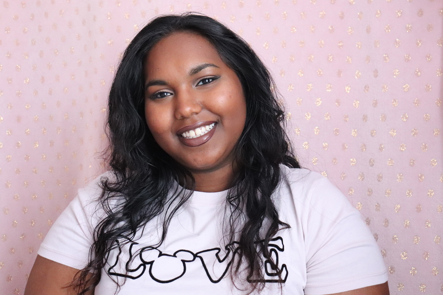 Ela. Long curly hair, wearing a white t-shirt and smiling at camera.