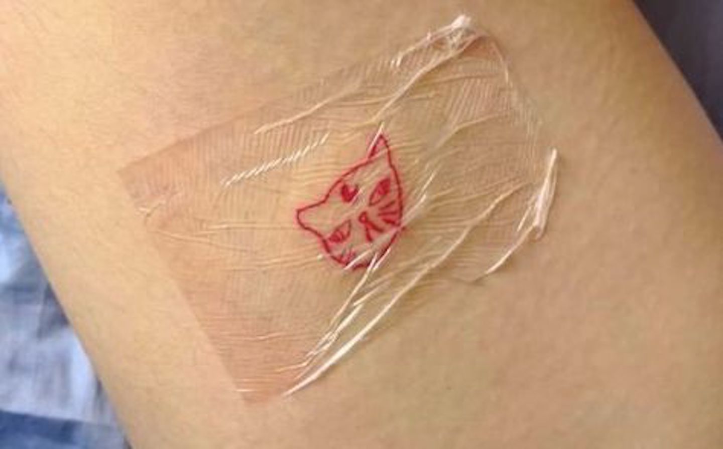 Ein kleines, rotes Stick-and-Poke-Tattoo zeigt eine Katze