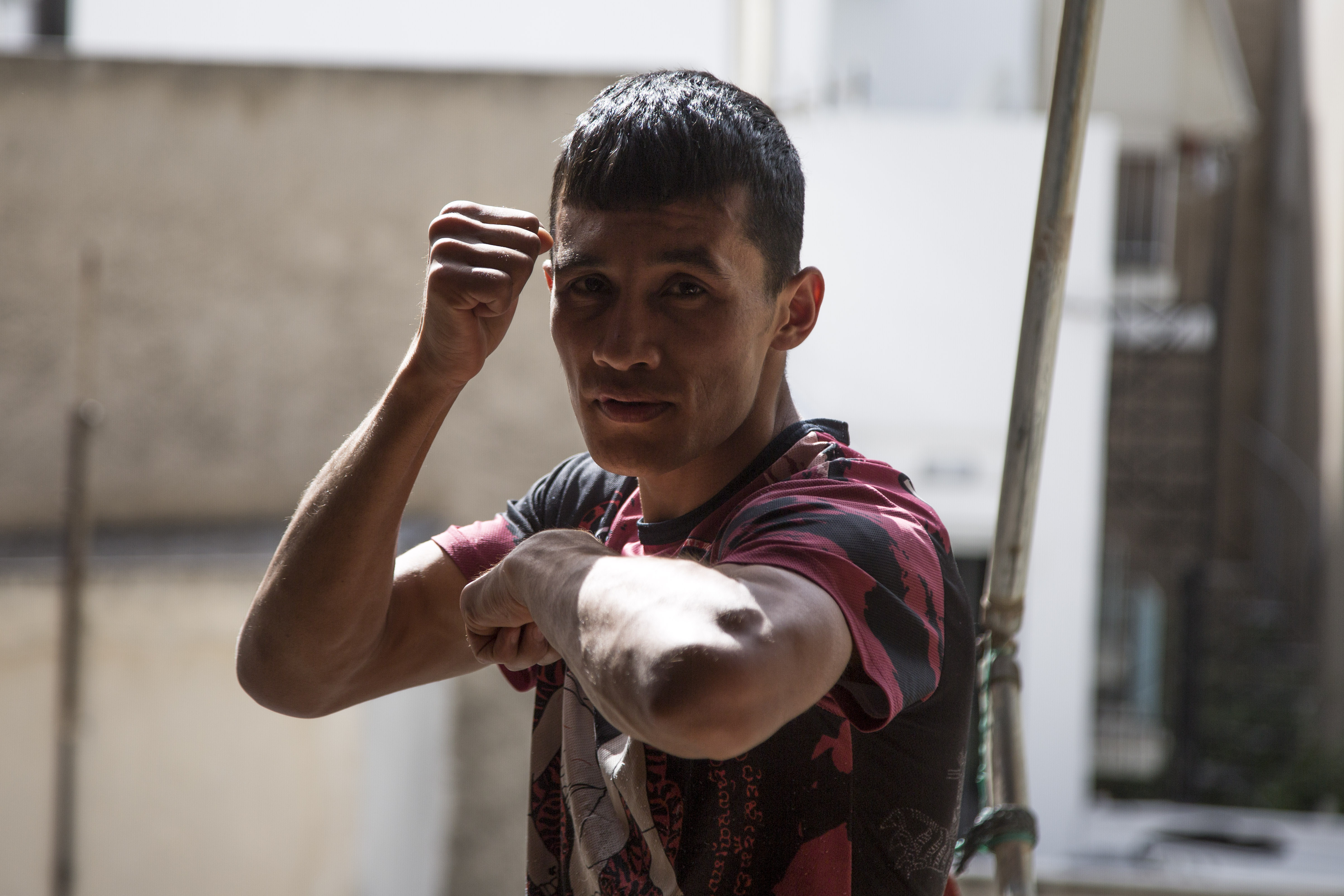 Majid Ahmadi - man wearing a red and black t-shirt, holding up one elbow parallel to the ground and one arm next to his face while looking at camera.