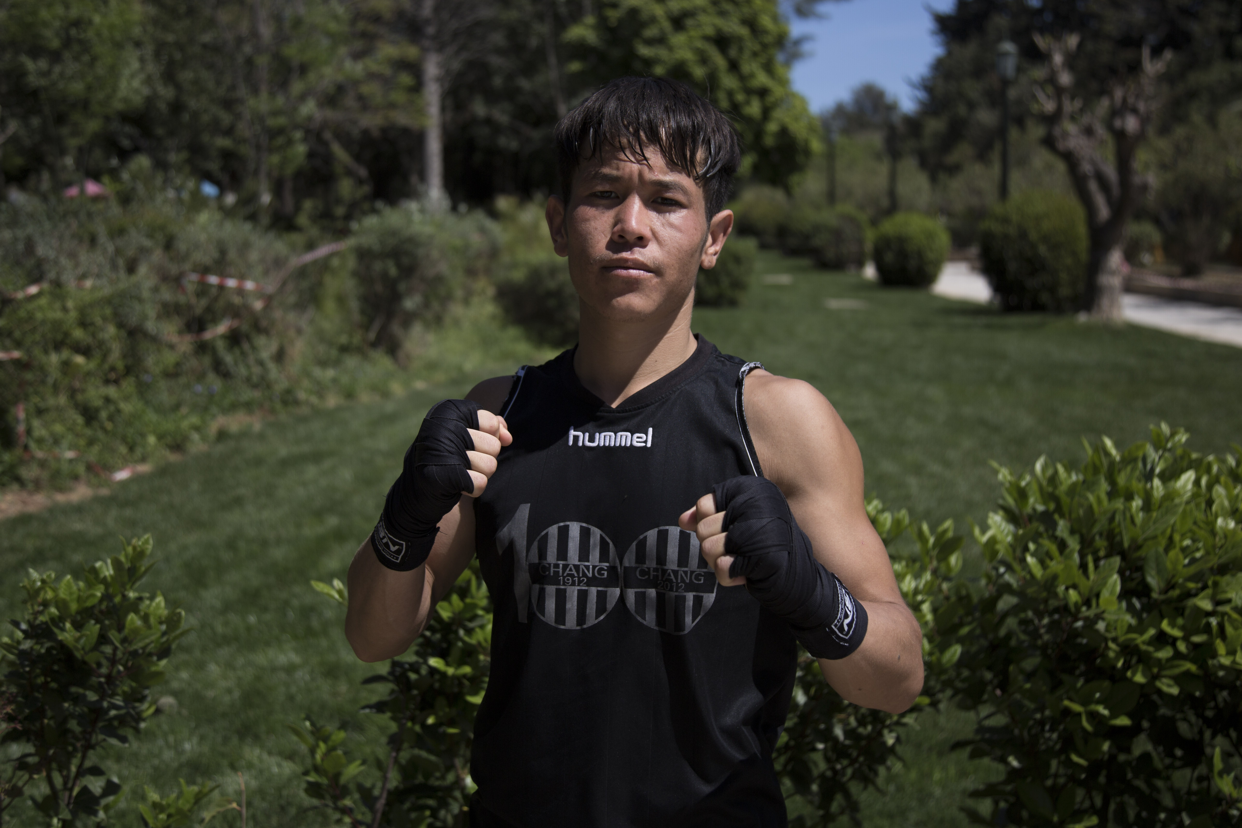 SHABIR HASANI - muscular teenager in all black holding fists up and posing in the park.