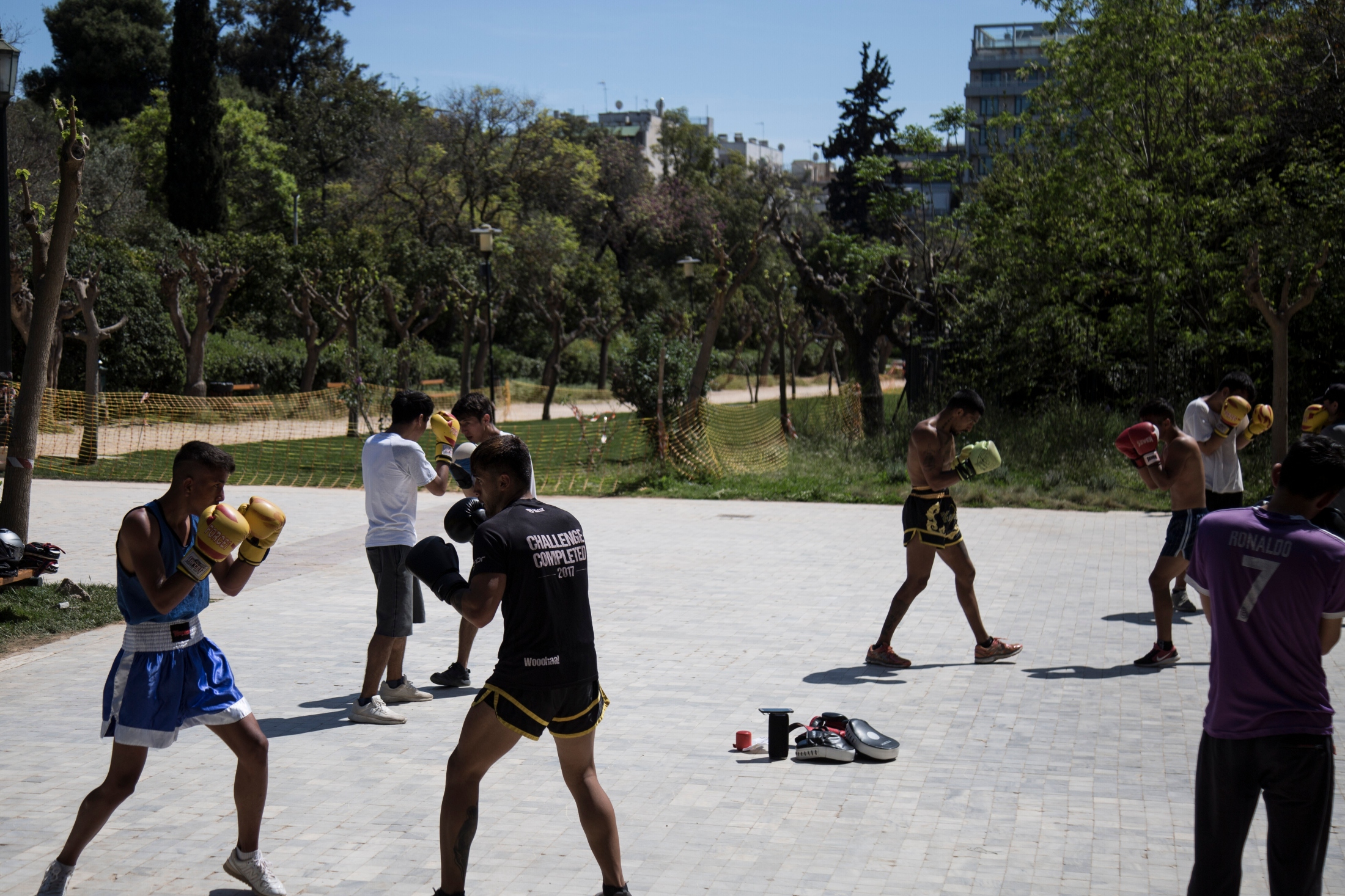 Yoga and Sports with Refugees - A group of young men wearing shorts and boxing gloves, training under the sun.