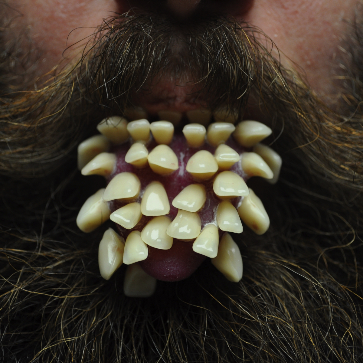 Foto di una lingua coperta di denti su una faccia umana con la barba.