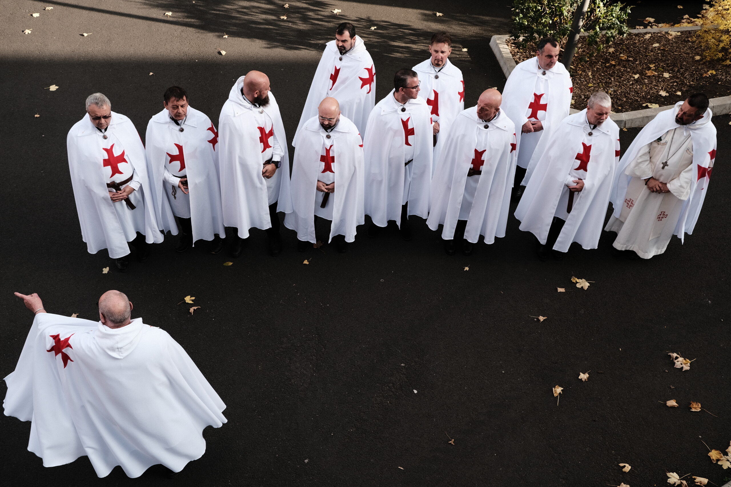 Zwölf Männer in weißen Templerroben auf einer Asphaltfläche