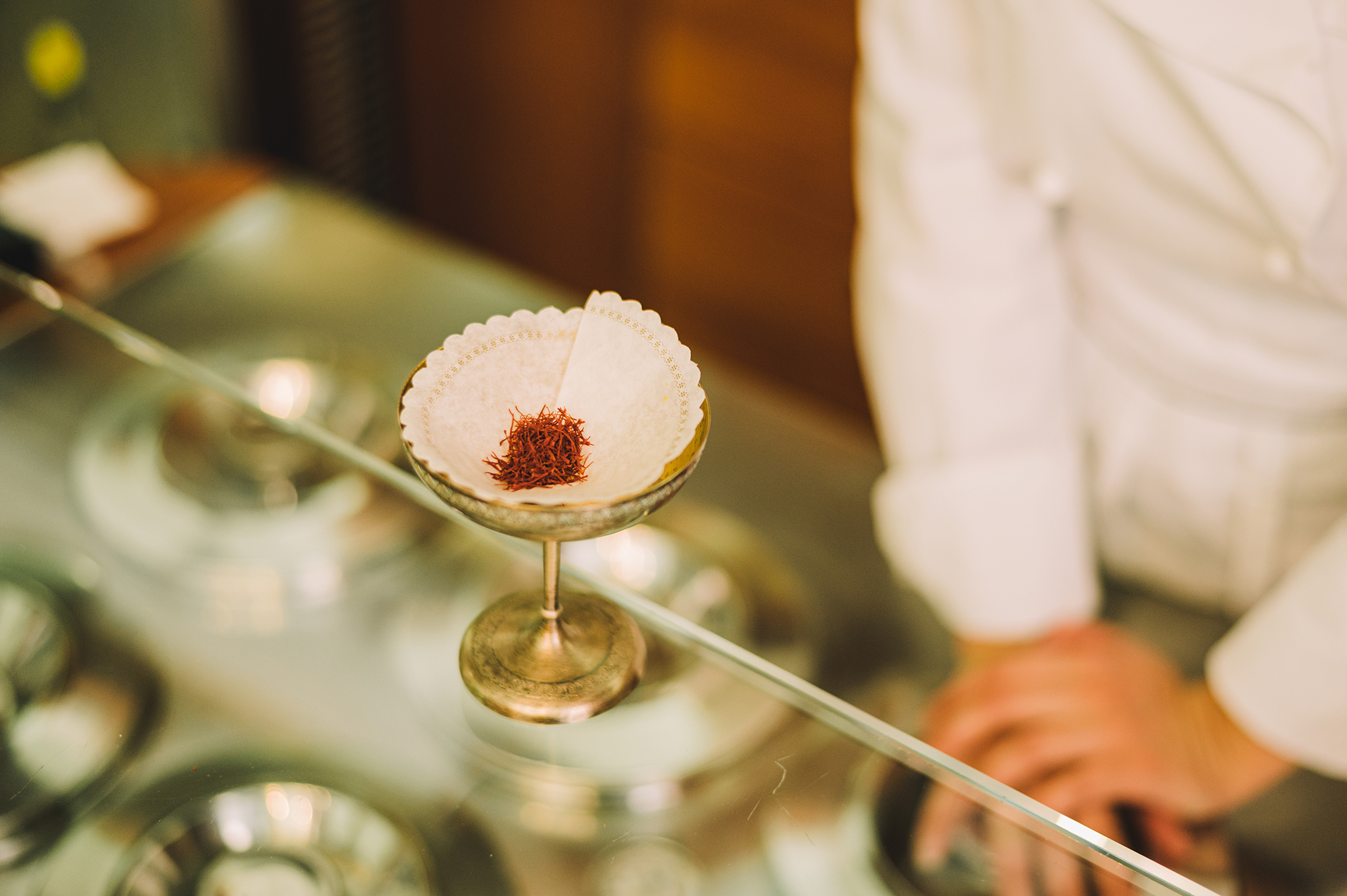 Mokambo, ice cream, Italy - Photograph of bright red saffron strands resting in a white paper filter in a golden goblet atop a glass cabinet.