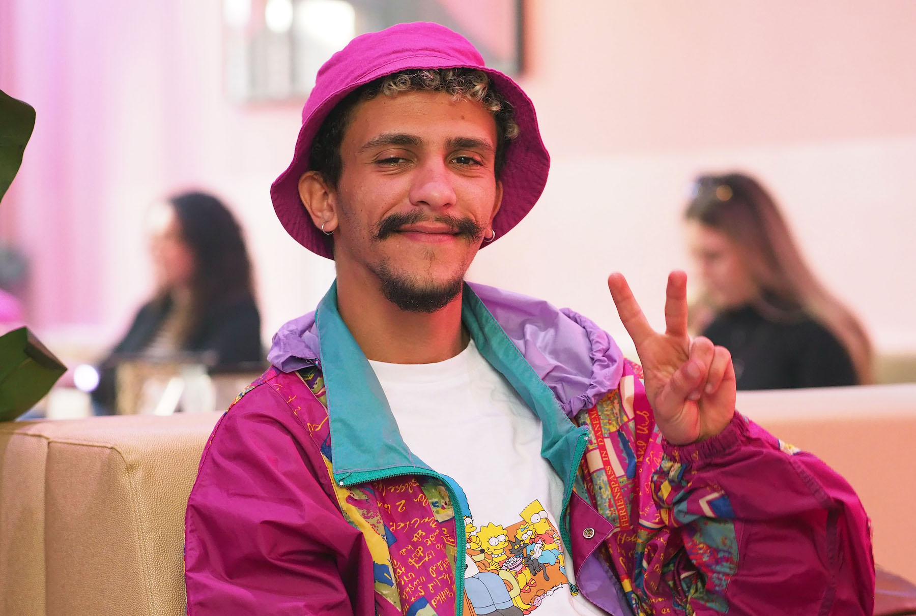 Uomo sorridente con cappello e giacca rosa, maglietta dei Simpson che guarda in camera