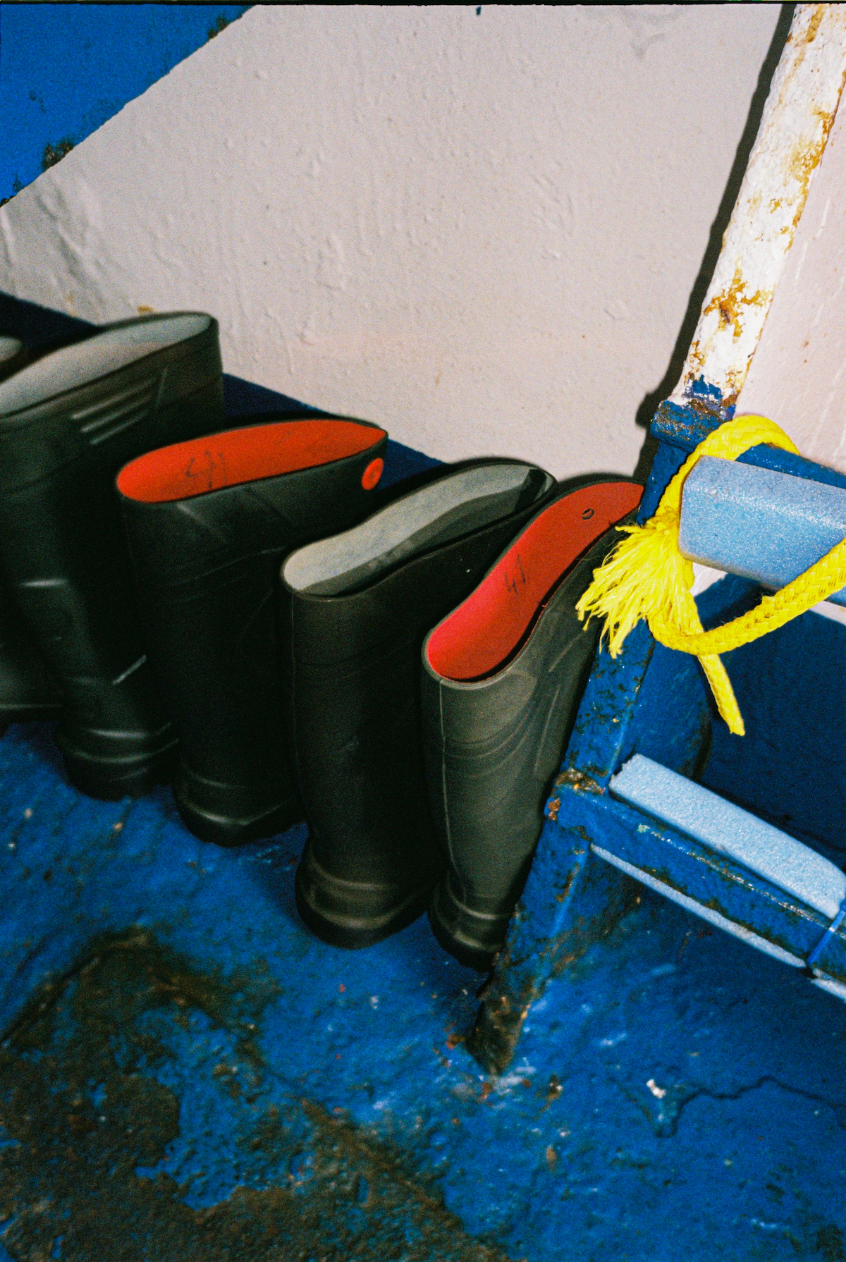 Ostend, fishing, photography - Photograph of two sets of rubber wellington boots placed on the dark blue floor of a boat.